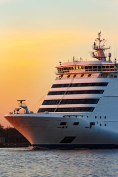 White passenger ship moving against the orange sunset sky