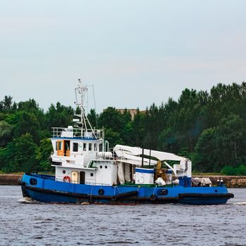 Blue tug ship moving to the cargo terminal. Industrial services