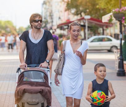 A family of four is taking time together with a walk downtown in a sunny summer day.