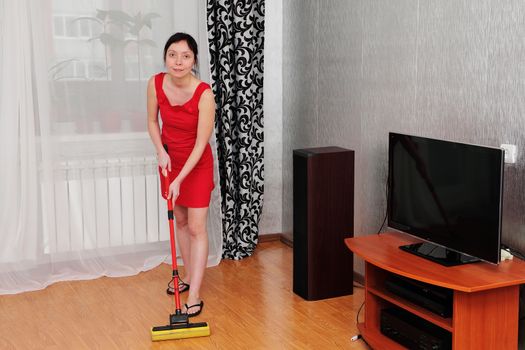 Beautiful woman makes wet cleaning of the room with a broom.