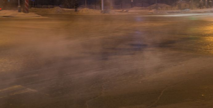 steam on the road, winter evening city asphalt vapor from the cold