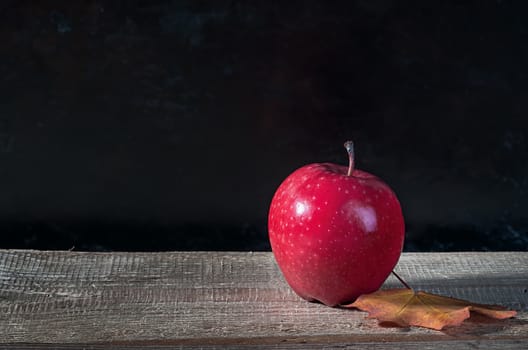 Red ripe apple on a wooden table. Autumn maple leaf. Dark background.