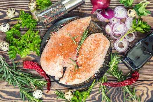 Raw uncooked chicken fillet on a cutting table with ingredients for cooking, on black plate. Top view. Toned.