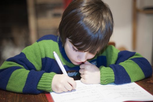 6 year old child performs homework on the kitchen wooden table