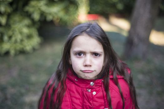 portrait of 7 year old girl in outdoor in the garden in winter with red jacket