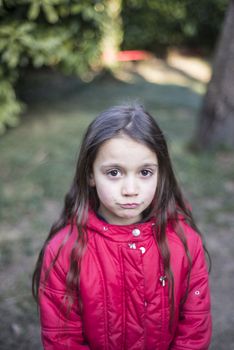 portrait of 7 year old girl in outdoor in the garden in winter with red jacket