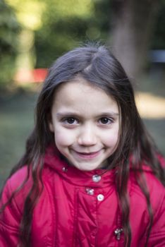 portrait of 7 year old girl in outdoor in the garden in winter with red jacket