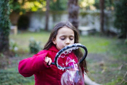 7 year old girl in outdoor in the garden in winter makes big soap bubbles