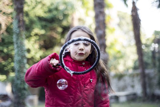 7 year old girl in outdoor in the garden in winter makes big soap bubbles