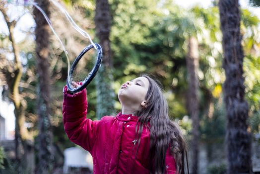 7 year old girl in outdoor in the garden in winter makes big soap bubbles