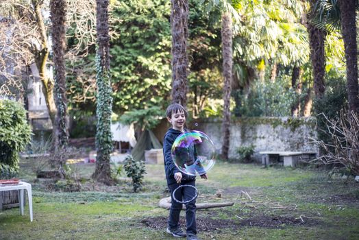 7-year-old child outdoors in the garden in winter makes big soap bubbles