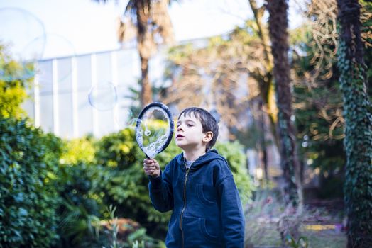 7-year-old child outdoors in the garden in winter makes big soap bubbles