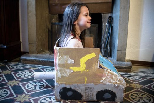 5-year-old girl plays with a self-made cardboard car, at home in her pajamas in the morning