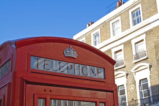 Red telephone booth in London over blue sky and in front of building