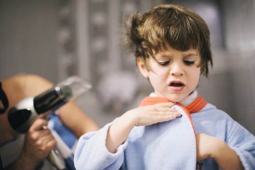 mother dries her son's hair with the hair dryer after the bath