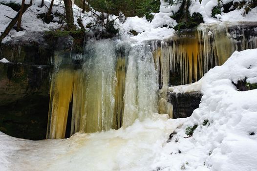 Frozen waterfalls on the rock, orange colored and snow