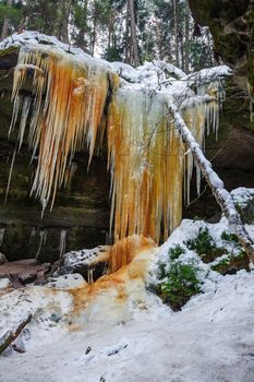 Frozen waterfalls on the rock, orange colored and snow
