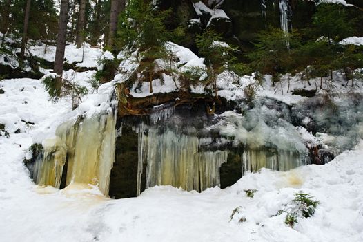 Frozen waterfalls on the rock, orange colored and snow