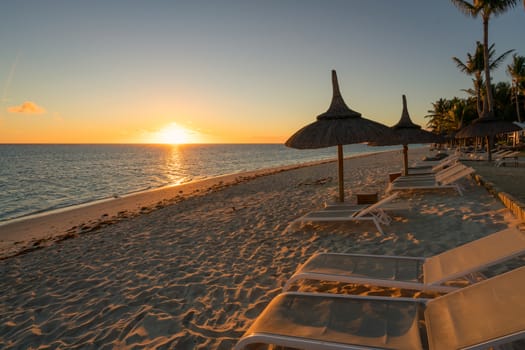 Amazing sunset, sandy beach with deckchairs and parasols typical of the Mauritius resorts