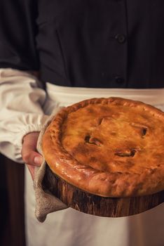 Pie from potato meat cheese and vegetables. Freshly baked pie in hands of woman in uniform