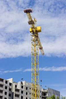 Tower crane with latticed boom on the background of the upper part of a multi-story residential building under construction and sky
