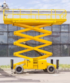 Yellow scissor wheeled lift on an asphalt ground on the background of the industrial building
