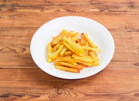 French fries on the white dish on a surface of old wooden planks 
