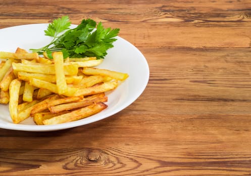 Fragment of the white dish with French fries and several twigs of parsley on a surface of old wooden planks 
