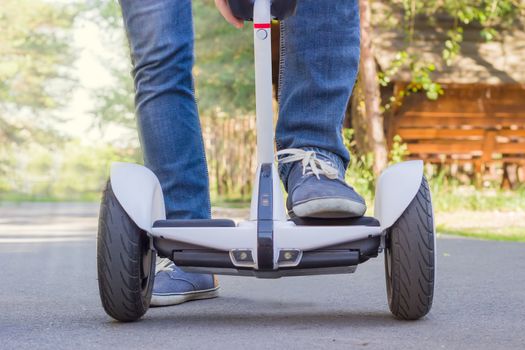 Legs of young man in blue jeans stepping on a segway on a asphalt walkway
