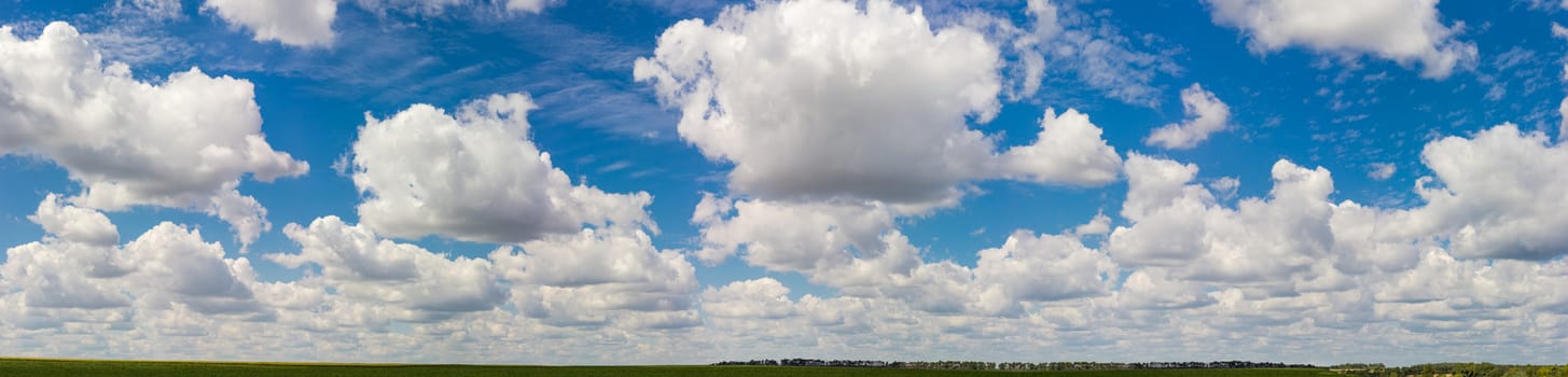 Big panorama of the sky with cumulus and cirrus clouds over a agricultural grounds and forest at summer day
