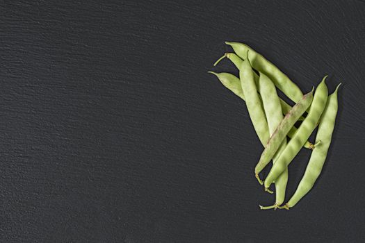 Pods fresh green beans on a black stone surface.  Top view, copy space. Healthy eating concept.