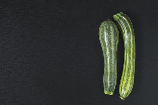 Two striped fresh green zucchini on a black stone surface.  Top view, copy space. Healthy eating concept.