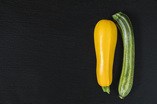 Striped fresh green zucchini and yellow zucchini on a black stone surface.  Top view, copy space. Healthy eating concept.