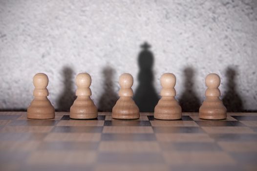 Chess king shadow standing out in a row of pawns