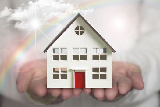Small house in a hand with sun clouds and rainbow 