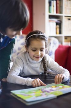 a 5 year old girl looks and reads a book with figures resting on the sofa of her house