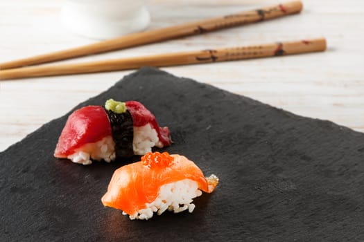 Salmon Nigiri with salmon roe on black slate stone with chopsticks and bowl of soy sauce. Raw fish in traditional Japanese sushi style. Horizontal image.