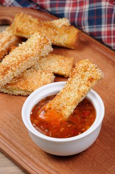 Slice of toast roasted in breaded with cheese and sesame slipped in a sauce on a wooden board