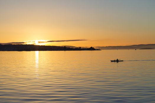 A man in silhouette kayaks across Oslofjord at sunset.