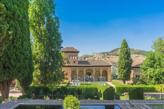 El Partal. A large central pond faces the arched portico behind which stands the Tower of the Ladies, inside the Alhambra of Granada, Andalusia, Spain, Europe on a bright sunny day with clear blue sky