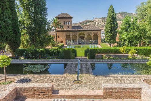 El Partal. A large central pond faces the arched portico behind which stands the Tower of the Ladies, inside the Alhambra of Granada, Andalusia, Spain, Europe on a bright sunny day with clear blue sky