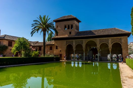 Alhambra de Granada, Spain - June 23, El Partal. A large central pond faces the arched portico behind which stands the Tower of the Ladies, inside the Alhambra of Granada, Andalusia, Spain, Europe on a bright sunny day with clear blue sky