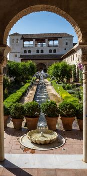 View of The Generalife courtyard, with its famous fountain and garden through an arch. Alhambra de Granada complex at Granada, Spain, Europe on a bright summer day