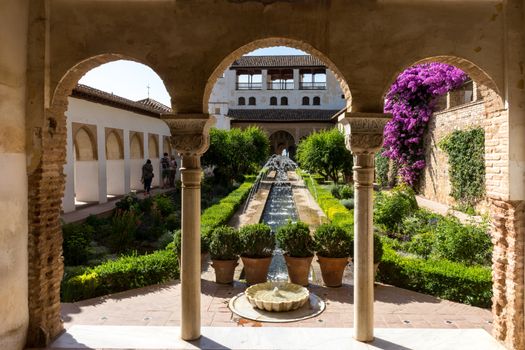 View of The Generalife courtyard, with its famous fountain and garden through an arch. Alhambra de Granada complex at Granada, Spain, Europe on a bright summer day