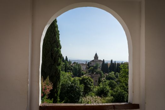 View of the bell tower of the Alhambra through the arched window from the Generalife gardens in Granada, Spain, Europe on a bright summer day