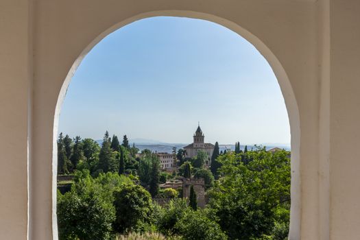 View of the bell tower of the Alhambra through the arched window from the Generalife gardens in Granada, Spain, Europe on a bright summer day