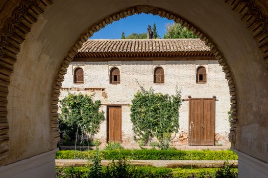 View of The Generalife courtyard, with its famous fountain and garden through an arch. Alhambra de Granada complex at Granada, Spain, Europe on a bright summer day