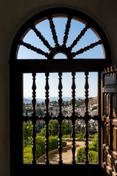 View of the Albayzin district of Granada, Spain, from an arched window grill in the Alhambra palace near sunset at Granada, Spain, Europe on a bright sunny day