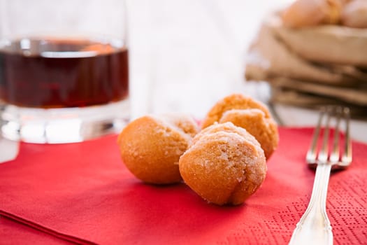 Closeup of castagnole, typical Italian carnival sweet on a red napkin and a glass of liqueur