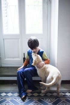 6 year old boy in pajamas with his golden retriever puppy dog in the house in front of the hall window